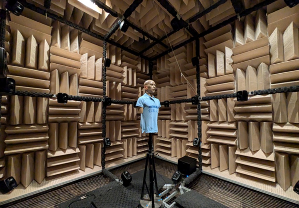 An anechoic recording chamber lined with acoustic foam wedges, with a KEMAR acoustic mannequin mounted on a tripod for hearing aid audio capture